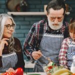 Grandparents and granddaughter preparing salad in home kitchen, creating memories together.